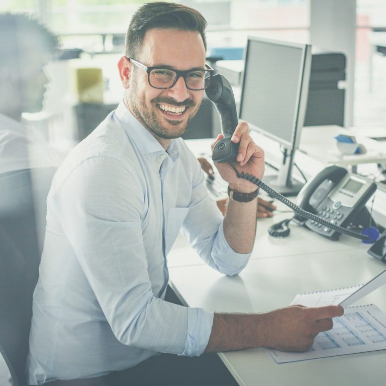 Homme étant au téléphone et tenant un document à la main tout en souriant.